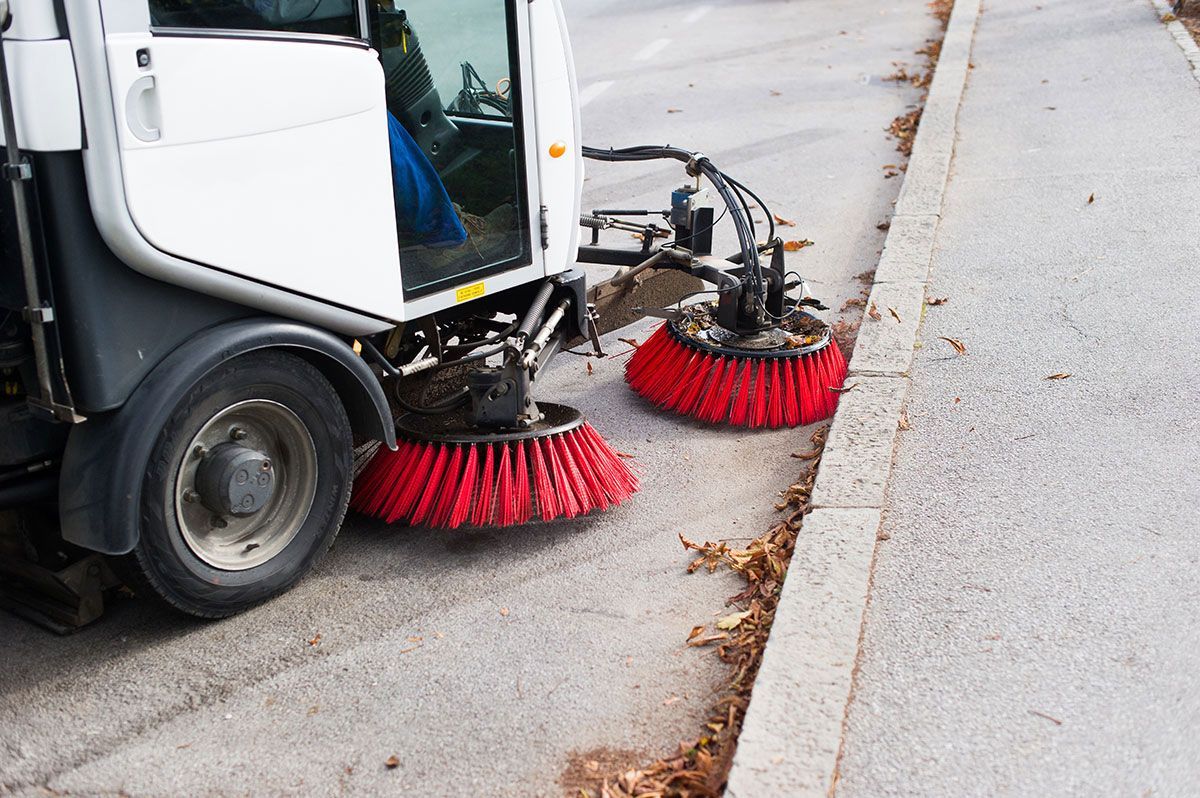 A street sweeper is cleaning the sidewalk with red brushes.