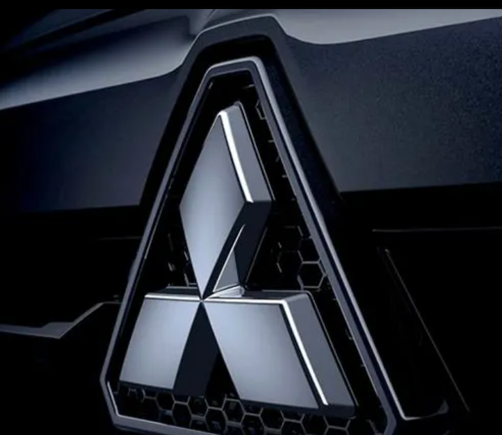 Logotipo da Mitsubishi em veículo escuro, emblema metálico dentro de uma grade hexagonal preta.