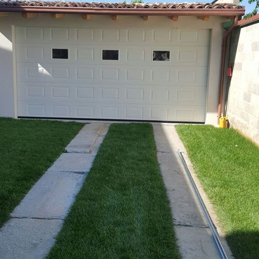 Una porta da garage bianca è posta accanto a un rigoglioso cortile verde.