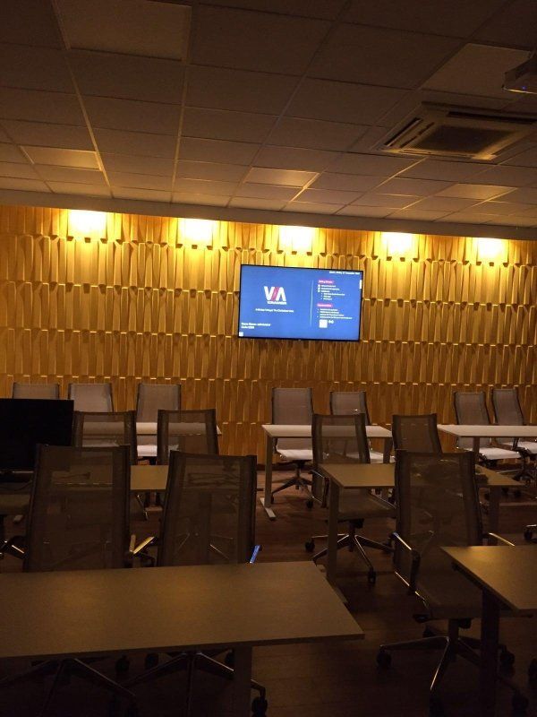 Un'aula con tavoli e sedie e una tv sul muro con la scritta va