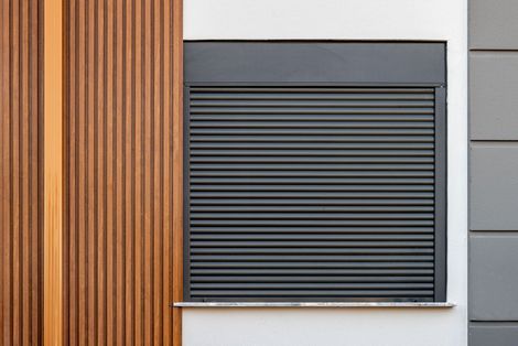 Esterno di un edificio con una persiana nera chiusa e pannelli in legno.