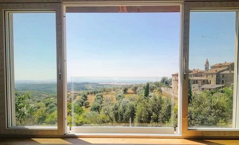Vista attraverso una finestra aperta: paesaggio verde, città in lontananza, cielo azzurro.