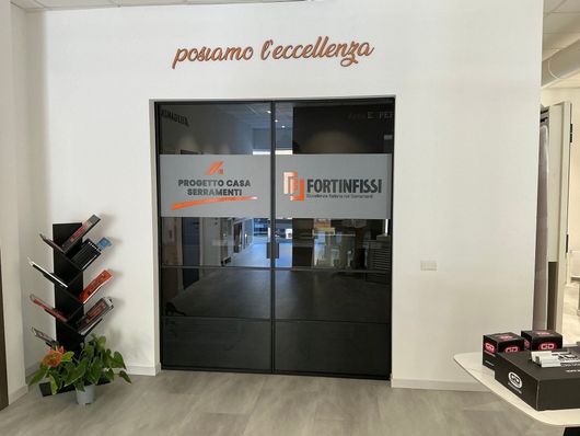 Showroom con vetrine e porte; persiane verdi, cornici bianche e grigie, parete decorativa arancione.