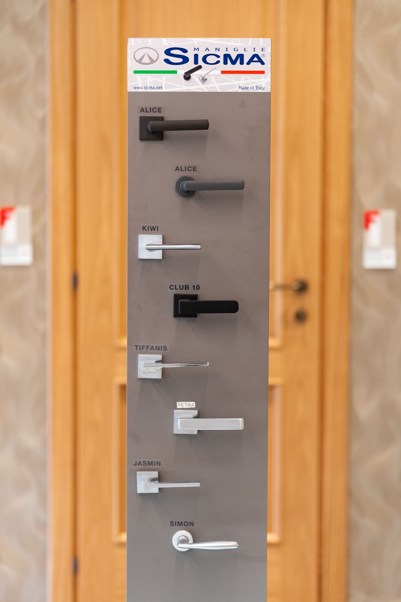 Esposizione di vari stili di maniglie per porte davanti a una porta in legno.