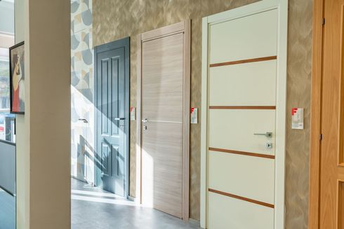 Tre porte interne: grigia, effetto legno chiaro e bianca con dettagli marroni, esposte in uno showroom.