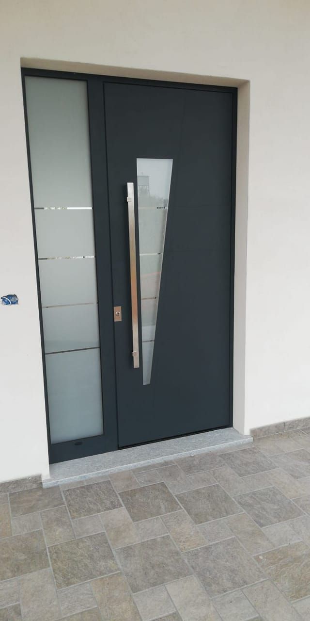 Porta d'ingresso grigio scuro con pannello in vetro smerigliato e maniglia in acciaio inossidabile.