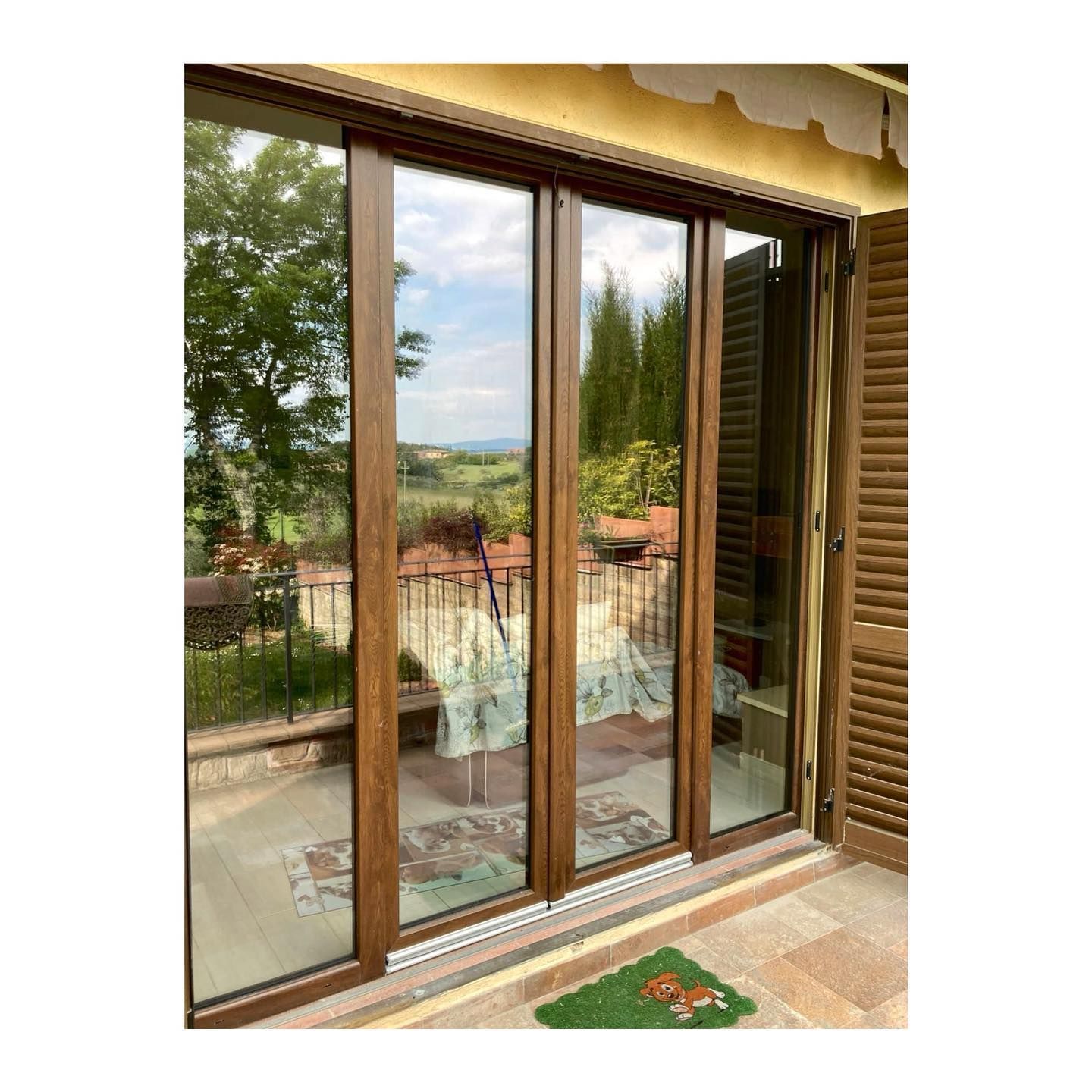 Le porte scorrevoli in vetro con cornice marrone si aprono su un balcone con vista sulla collina.