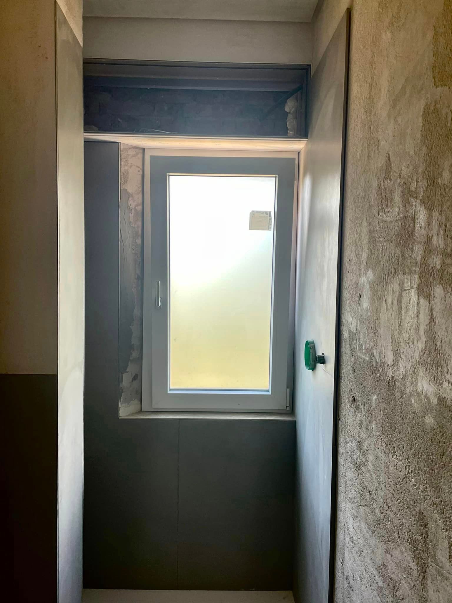 Corridoio stretto con una finestra rettangolare, circondato da pareti grezze.