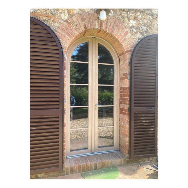 Portale ad arco con persiane in legno. Facciata in mattoni, porta in legno chiaro e finestra ad arco.