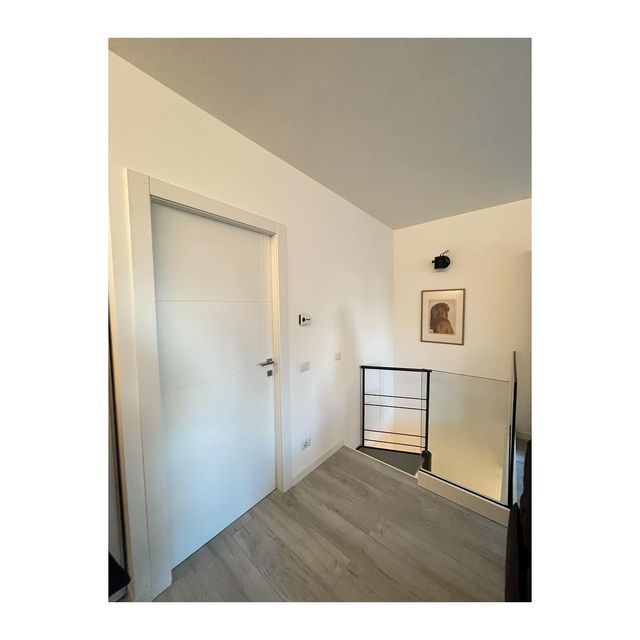 Corridoio interno con porta bianca, pavimento effetto legno chiaro e un quadro incorniciato sulla parete.