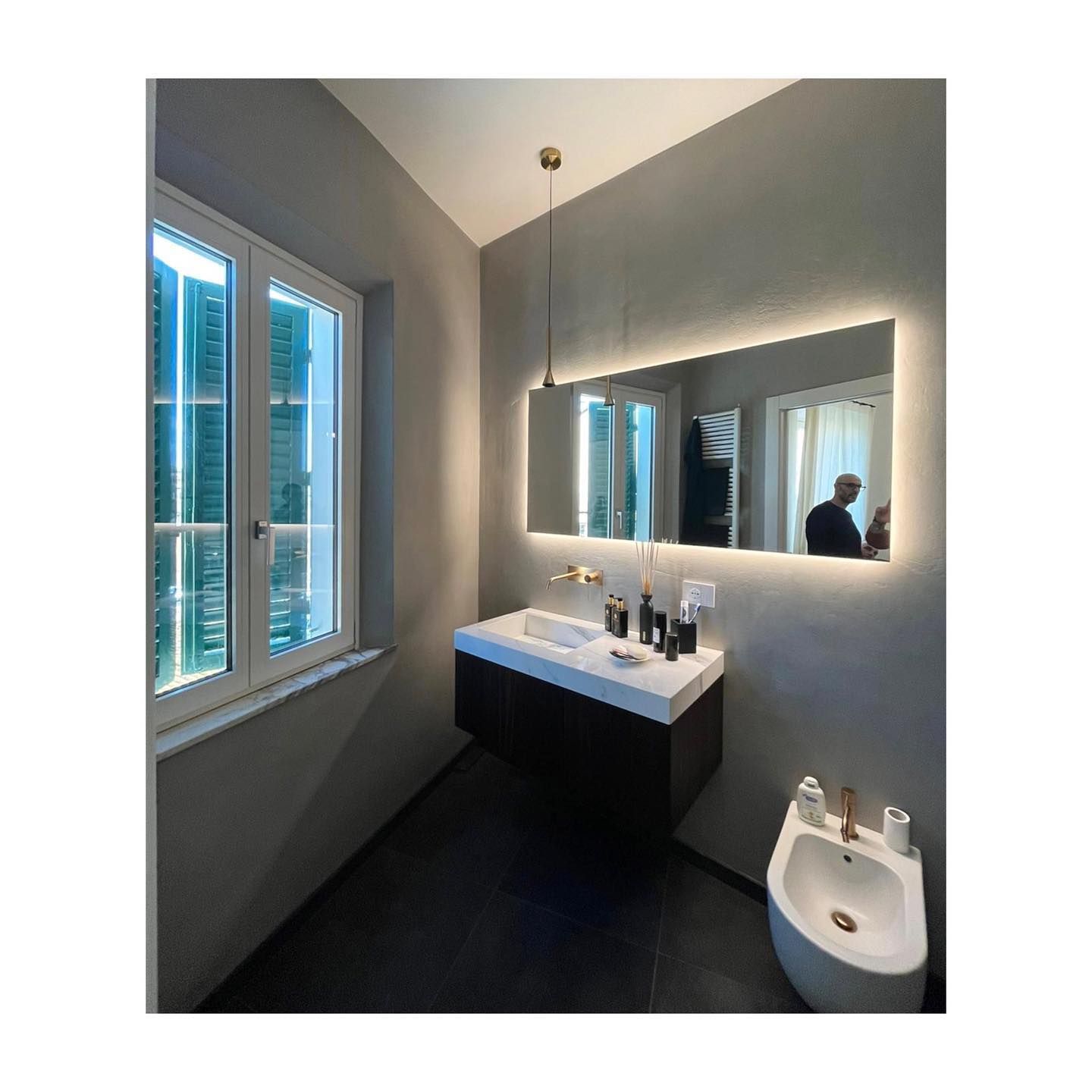 Bagno moderno con un grande specchio con illuminazione a LED, lavandino sospeso, finestra e bidet.