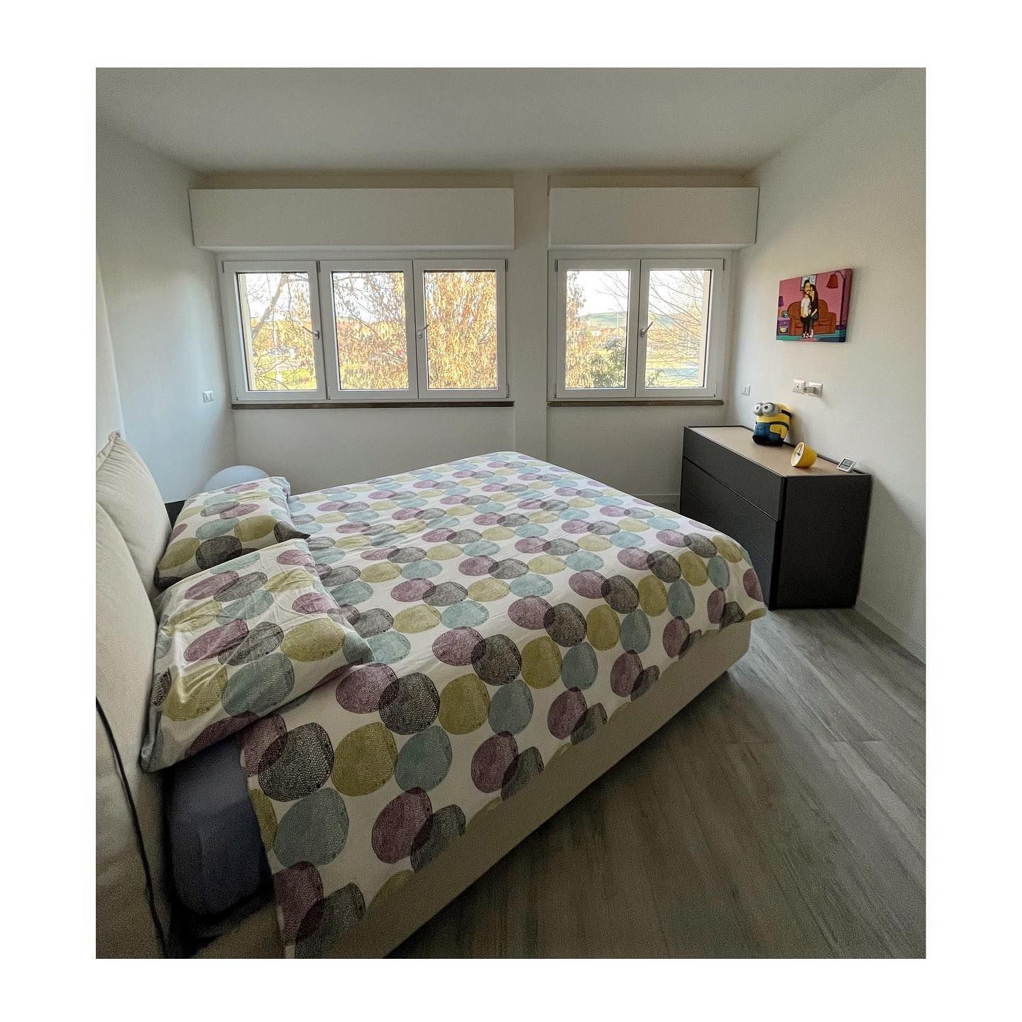 Camera da letto con letto, finestre, cassettiera e copriletto colorato.