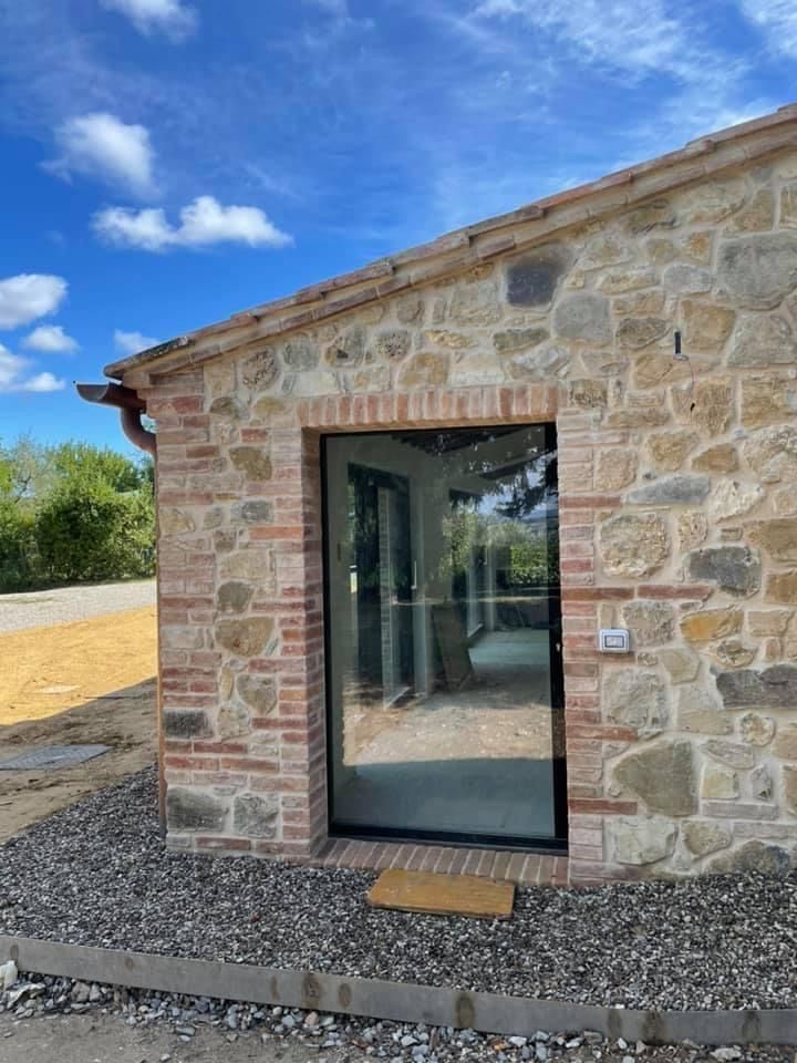 Edificio in pietra con porta a vetri, circondato da ghiaia. Cielo azzurro e limpido visibile.