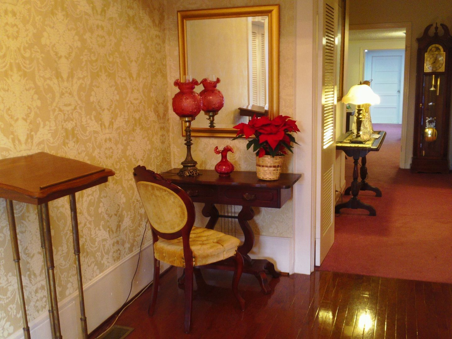 Hallway interior with table, chair, mirror, and clock; red flowers.