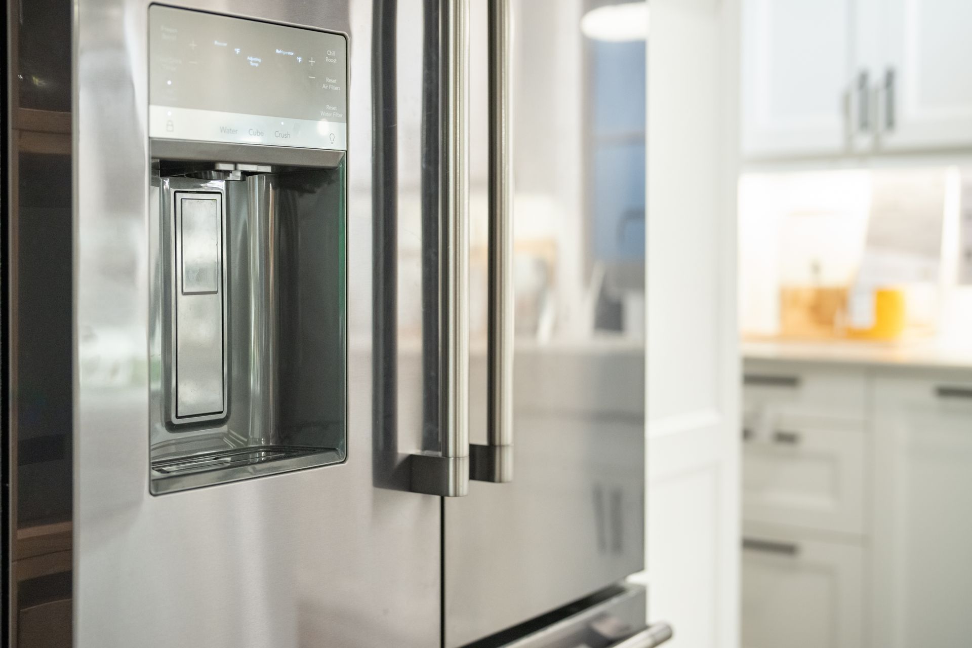 Close-up of a stainless steel refrigerator with a water dispenser; blurred kitchen background.