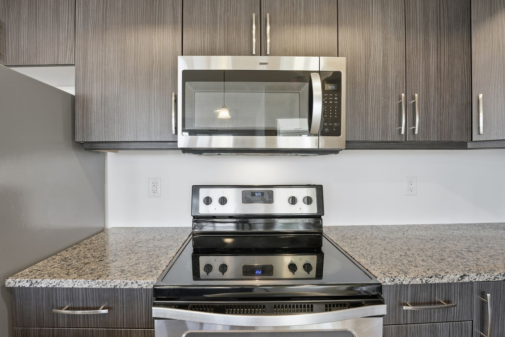Stainless steel microwave and stovetop in a kitchen with gray cabinets and granite countertop.