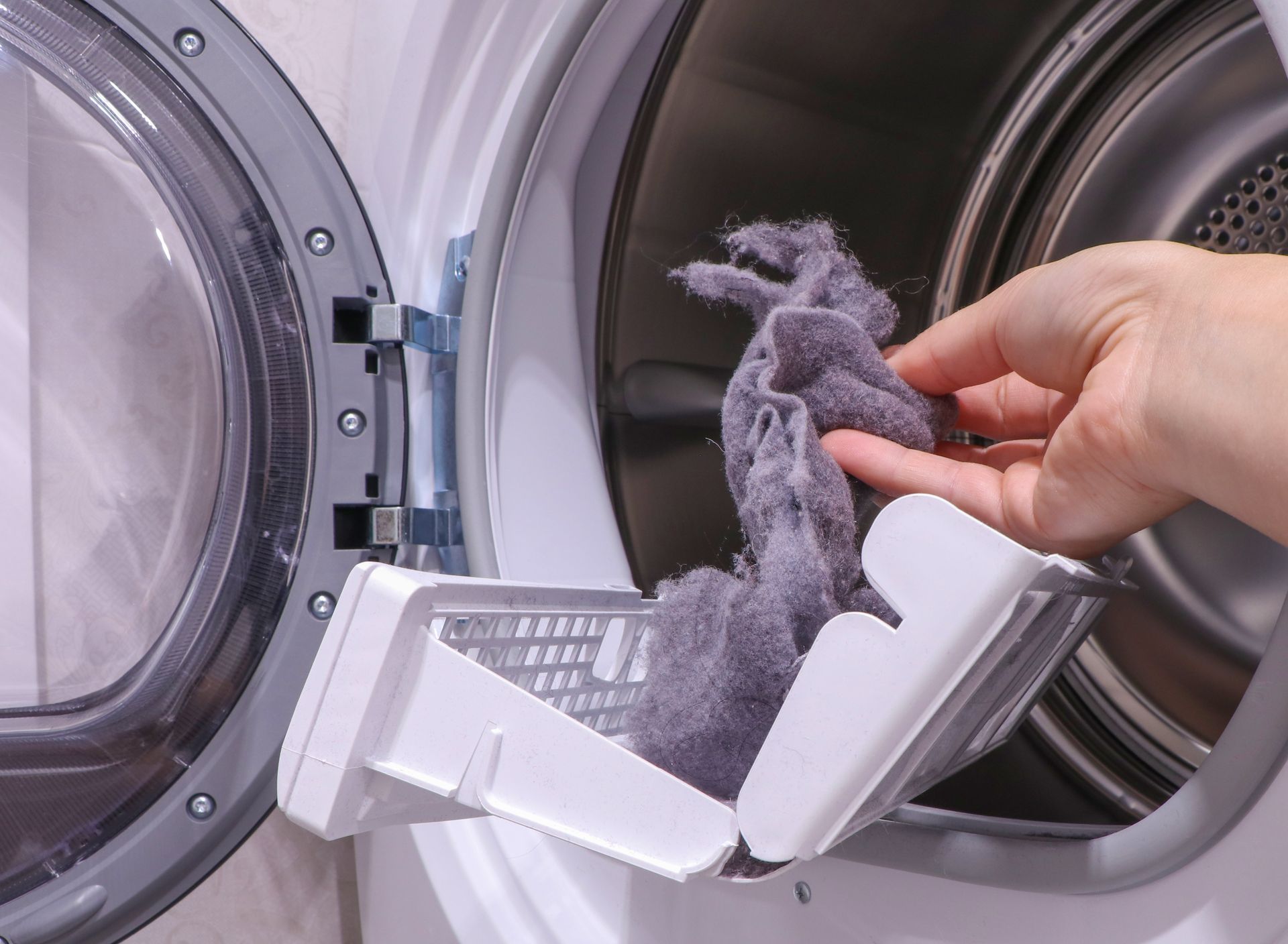 Hand removing lint from a dryer lint trap, white dryer, close-up.