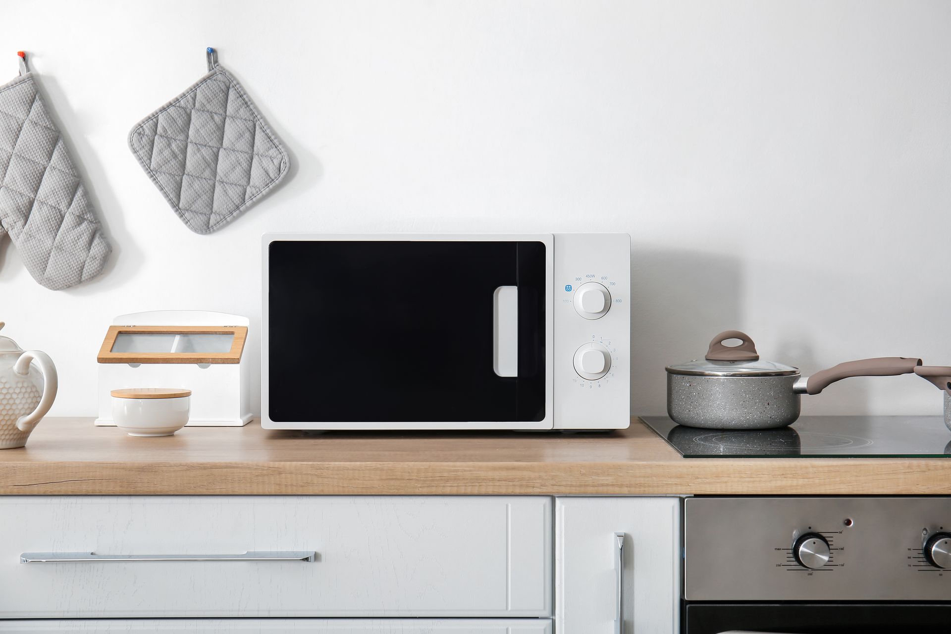 White microwave on a countertop in a kitchen. Pots and pot holders are nearby.
