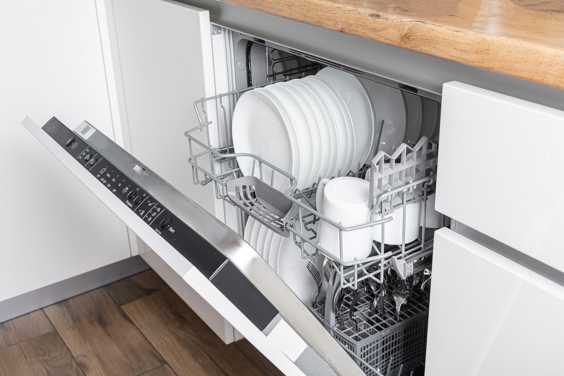 Dishwasher open, filled with white dishes and mugs; kitchen counter and cabinet visible.