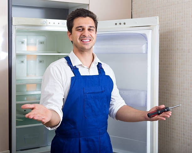 Appliance technician repairing refrigerator with screwdriver during professional fridge repair.
