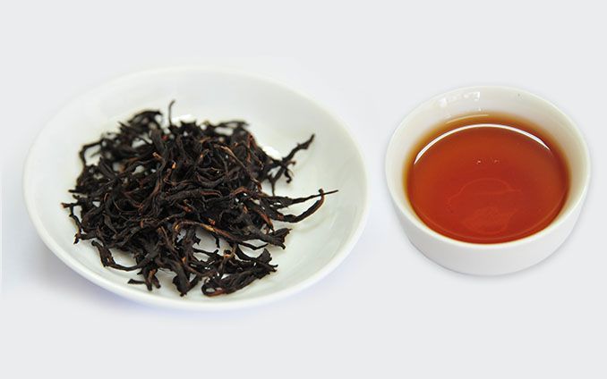 白色碟子裡盛著有機紅茶的茶葉，旁邊放著一杯深琥珀色的茶。