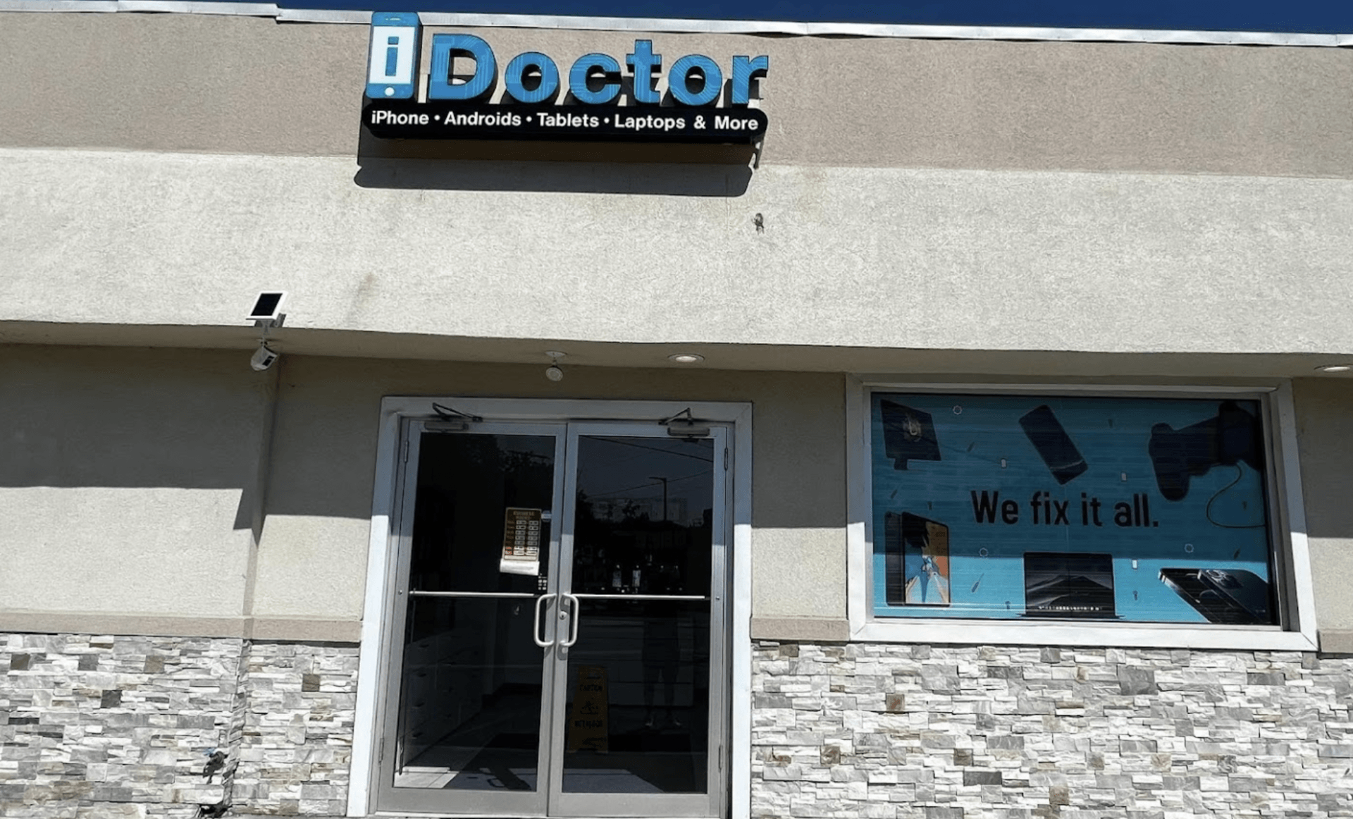 IDoctor storefront with glass double doors and blue window sign on a beige building