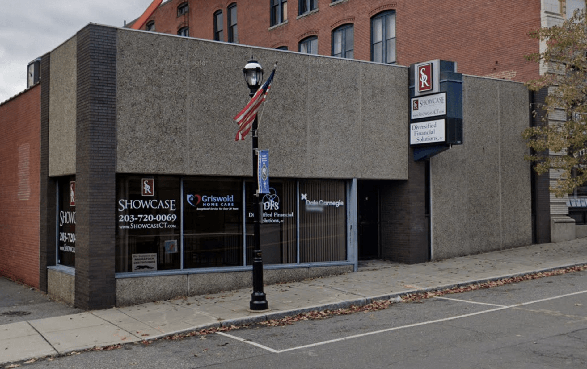 Street corner with a brick storefront, American flag sign, and parked car on an empty road.