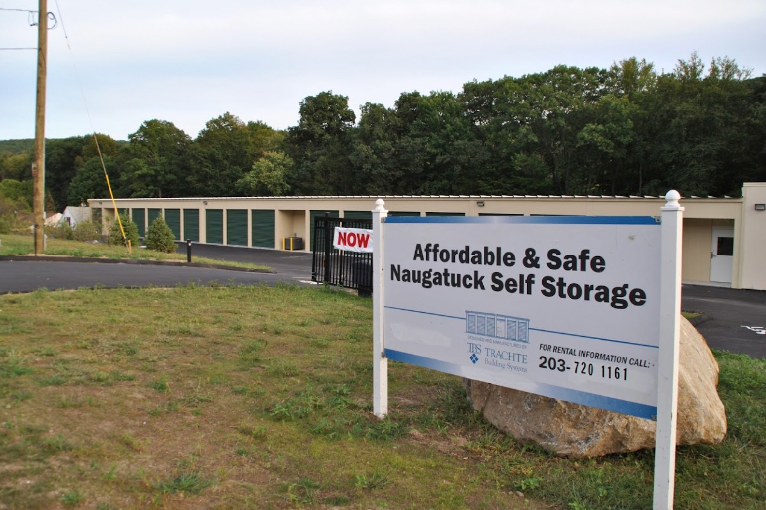 Affordable & Safe Naugatuck Self Storage sign beside low storage buildings and trees.
