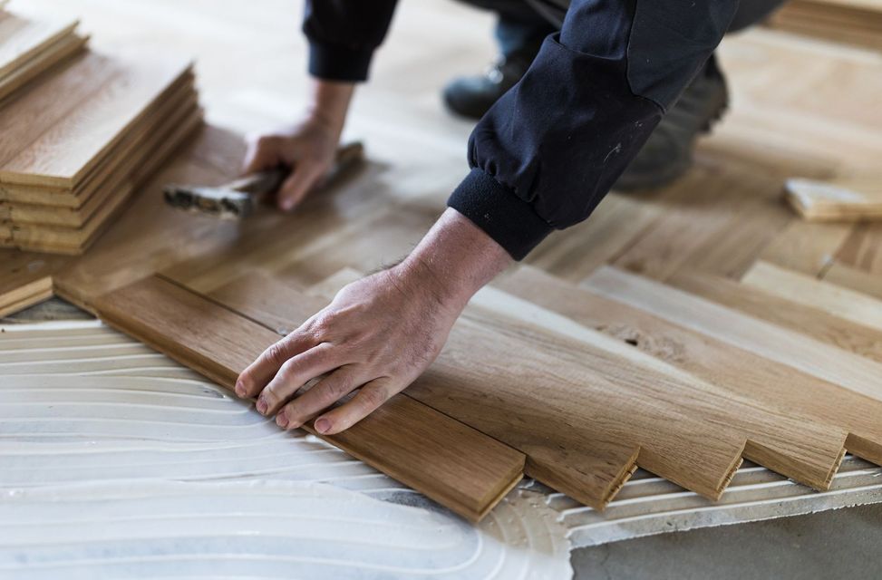 A person is laying wooden flooring on the floor.