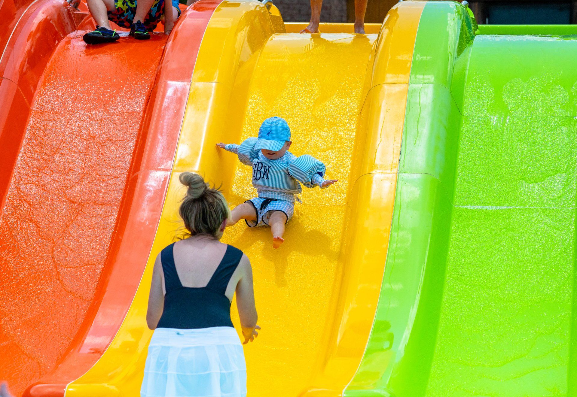 Child sliding down bright yellow slide while an adult watches on a colorful playground slide set