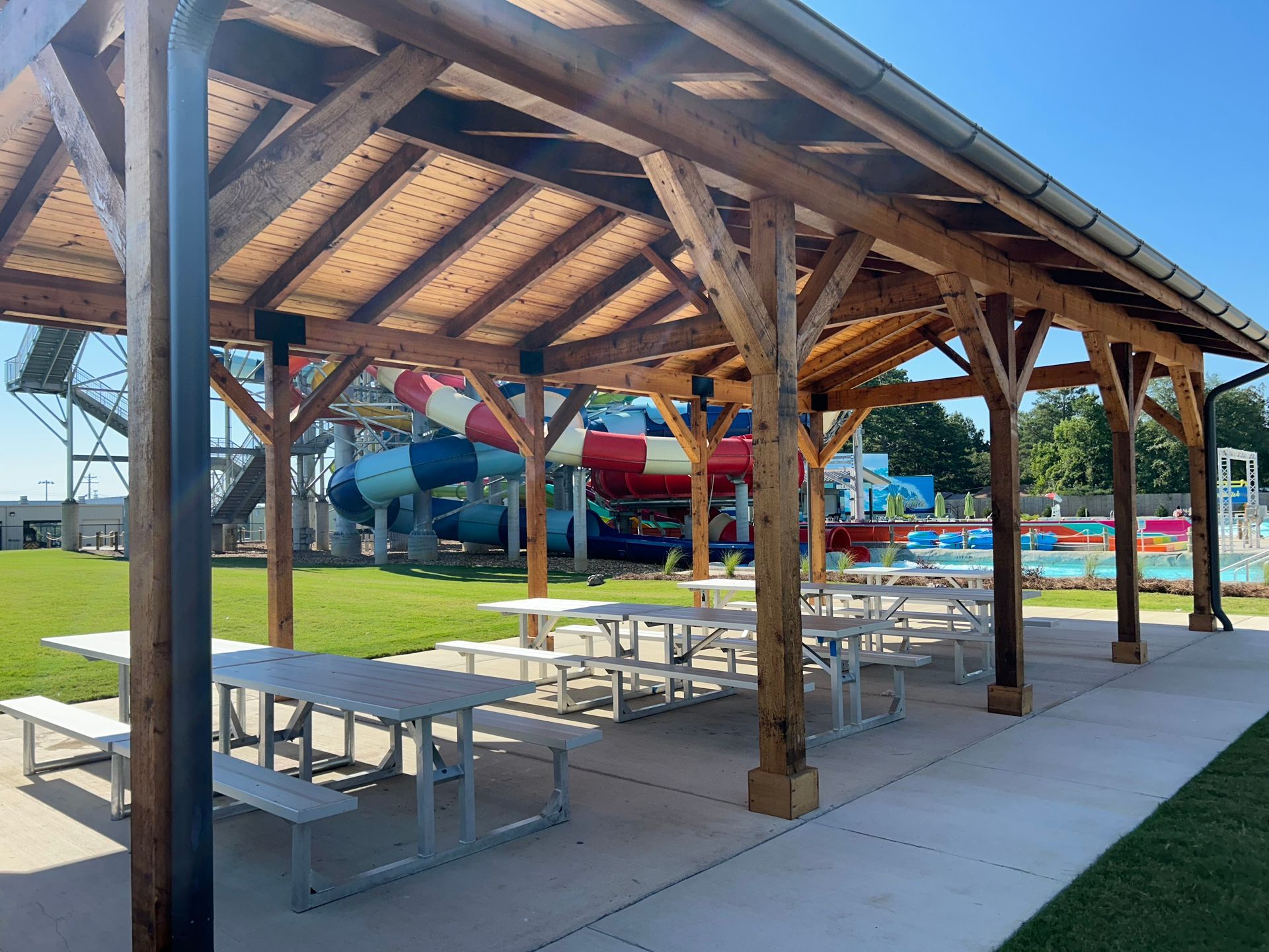Wooden pavilion with picnic tables beside a colorful outdoor splash park on a sunny day
