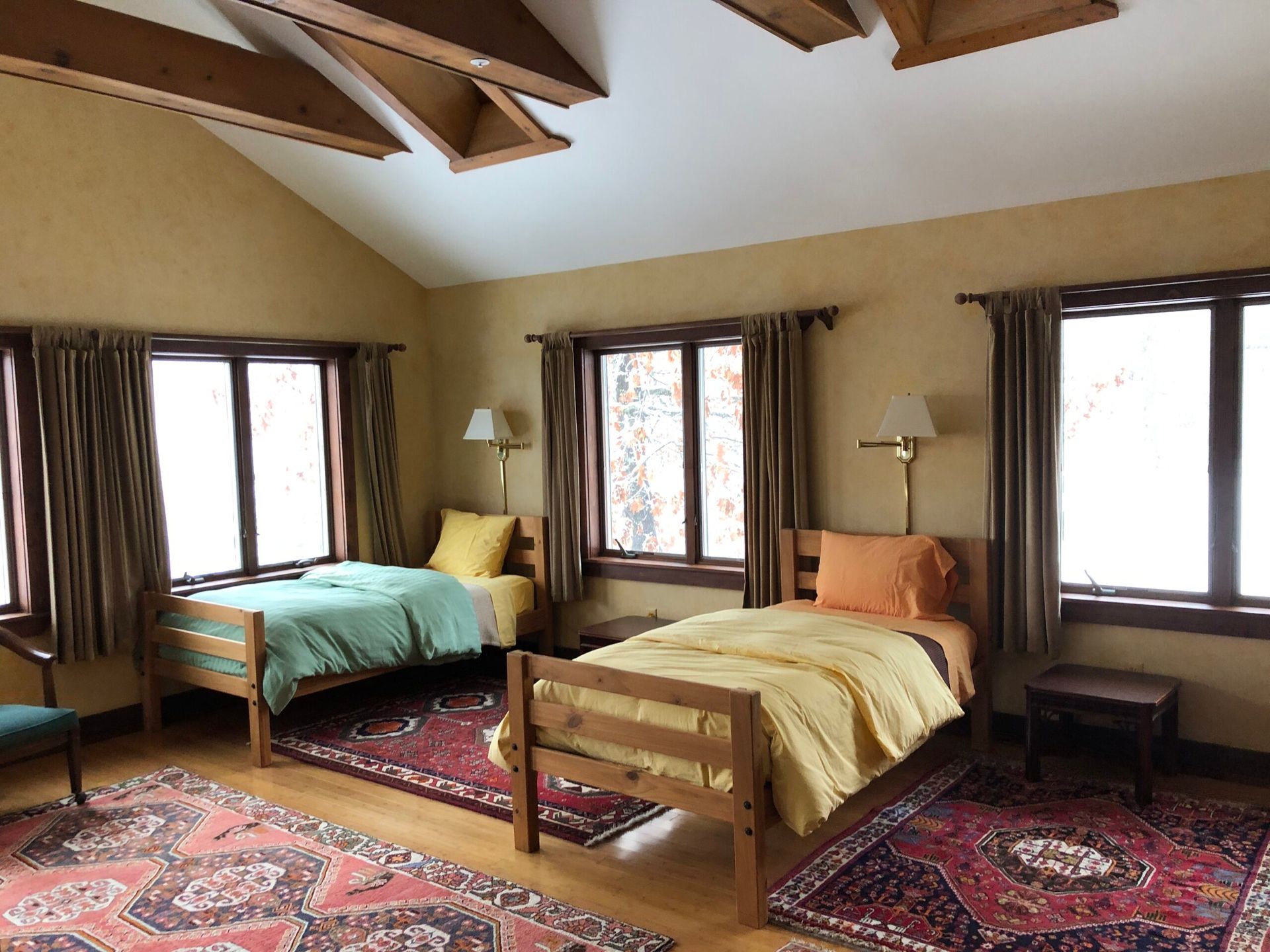Rustic bedroom with two single beds, exposed wood beams, and large windows with curtains