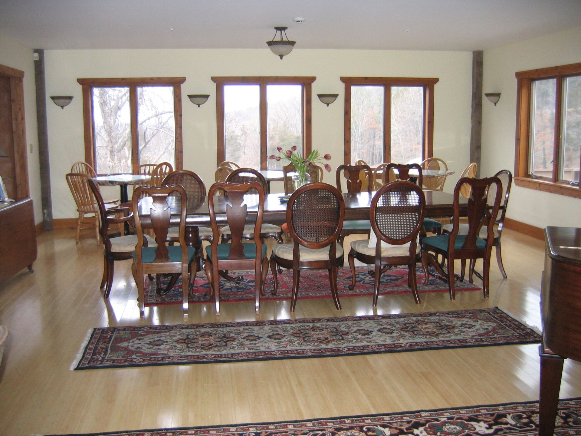 Dining room with a long table, wooden chairs, and large windows letting in daylight.