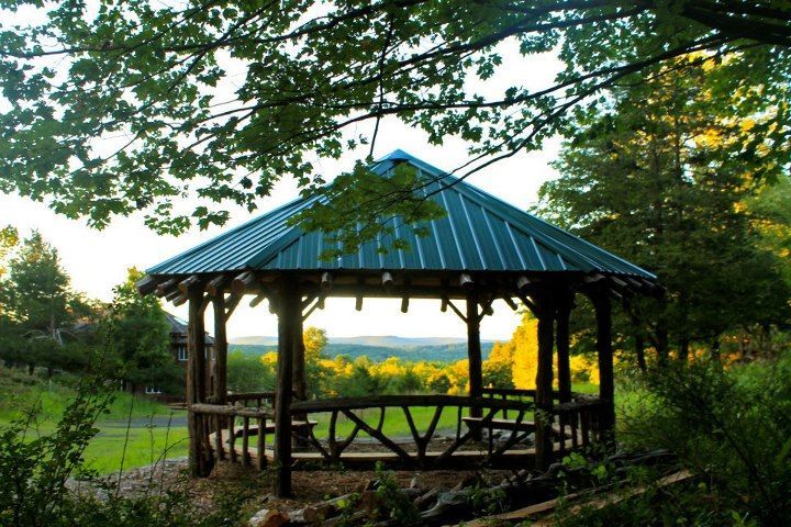 Wooden gazebo with a green metal roof in a park at sunset, framed by trees and grass