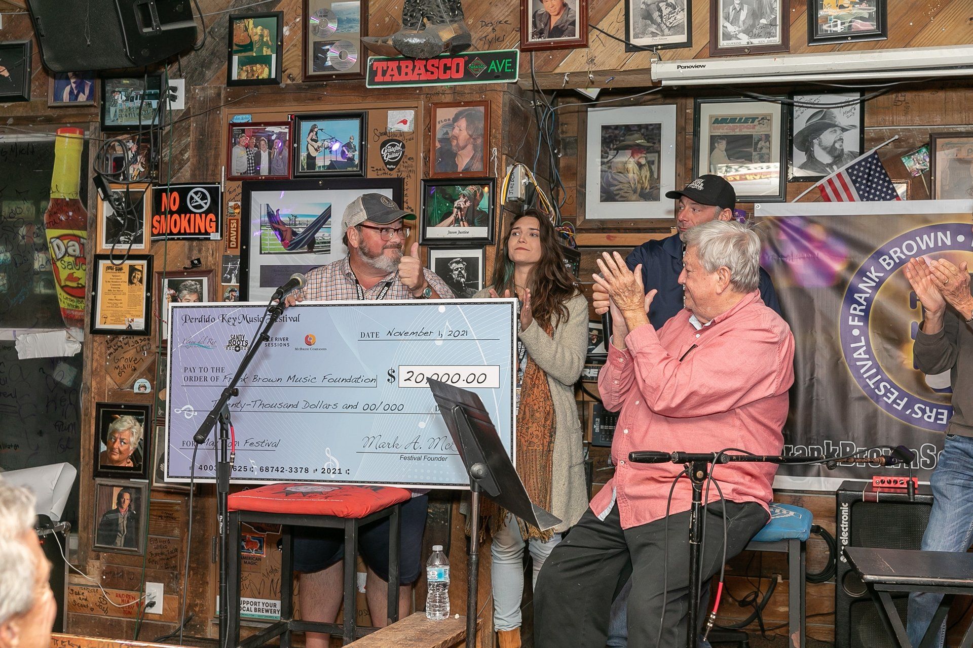 A group of people standing on a stage holding a large ceremonial check inside a rustic, memorabilia-filled venue.
