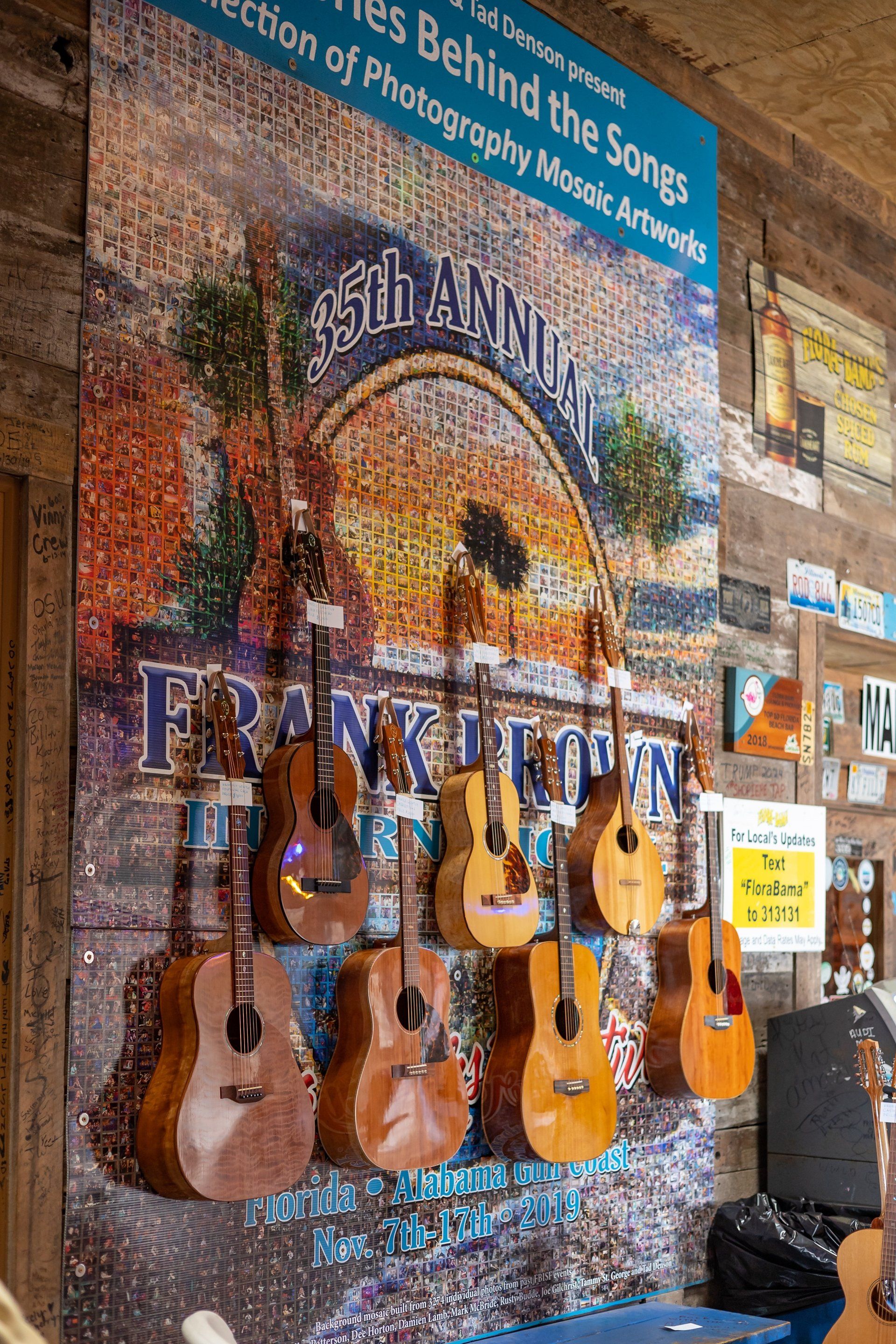 A display wall featuring hanging acoustic guitars over a large mosaic poster for the 35th Annual Frank Brown Songwriters Festival.