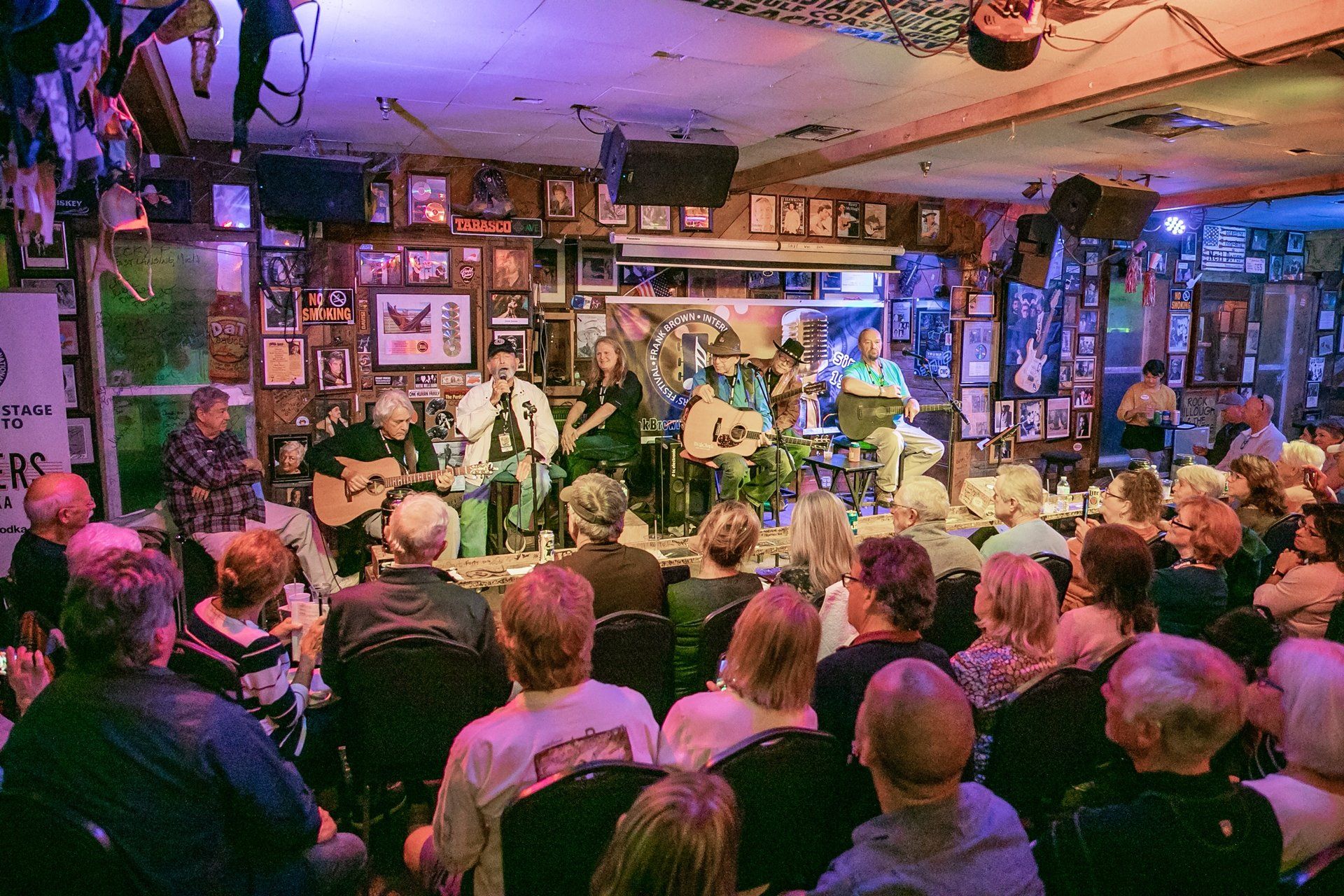 A crowd of people seated in a dim, wood-paneled venue watching several musicians perform on a small stage.