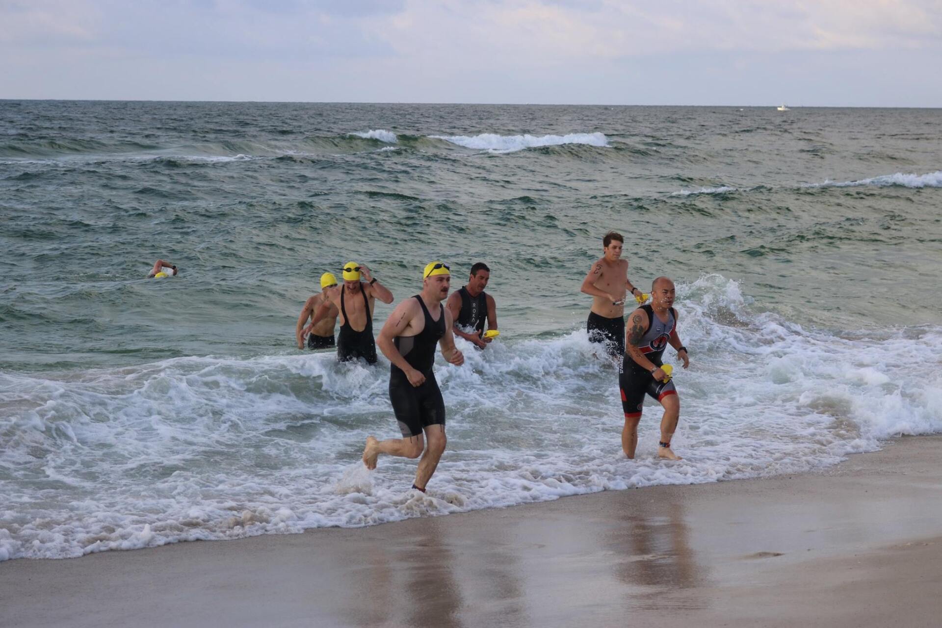 Athletes in swim gear emerge from ocean surf onto a sandy beach during a race.