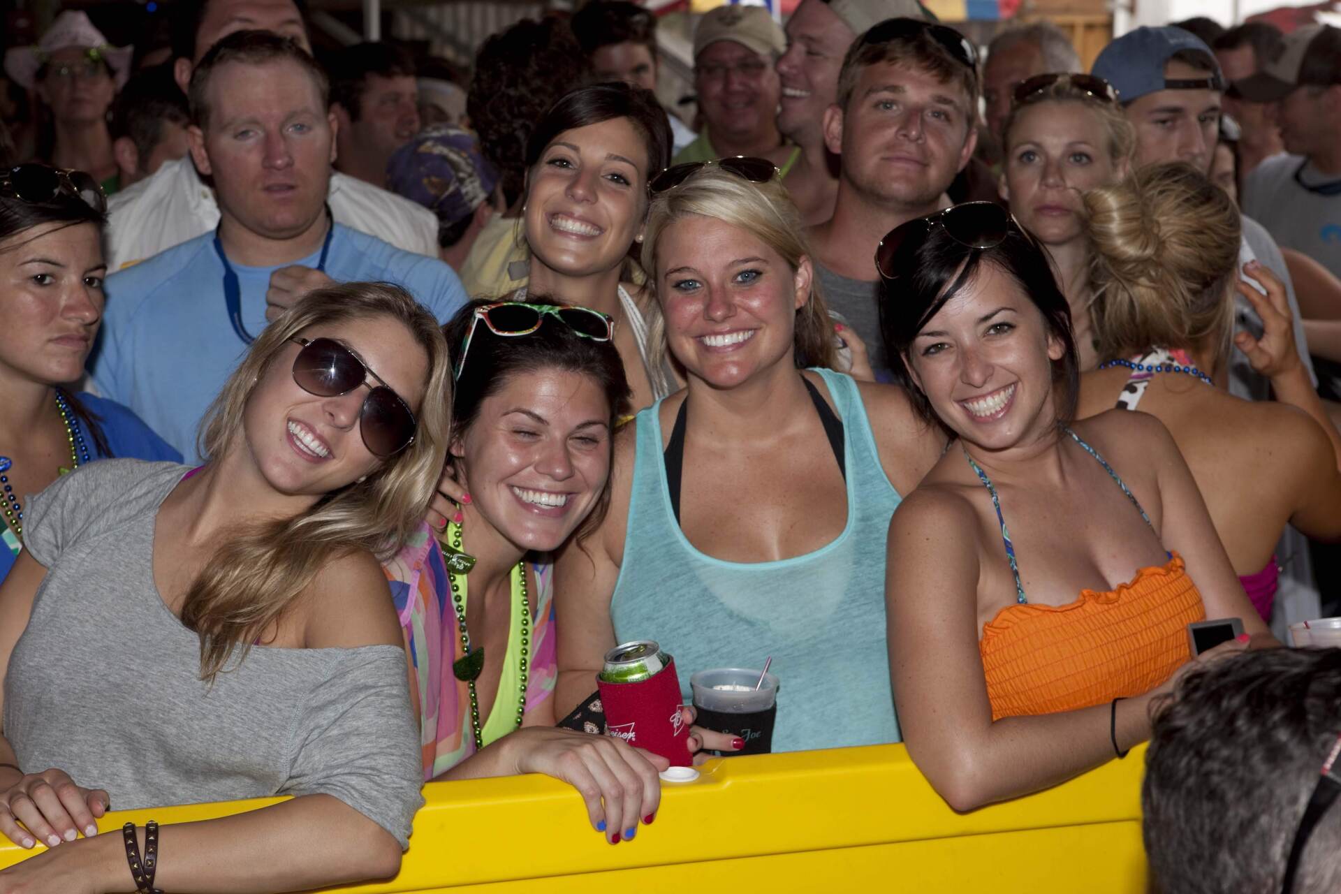 A group of smiling people stand behind a yellow railing at an outdoor event, looking toward the camera.