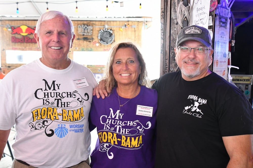 Three people smiling at the Flora-Bama bar. Two wear matching 