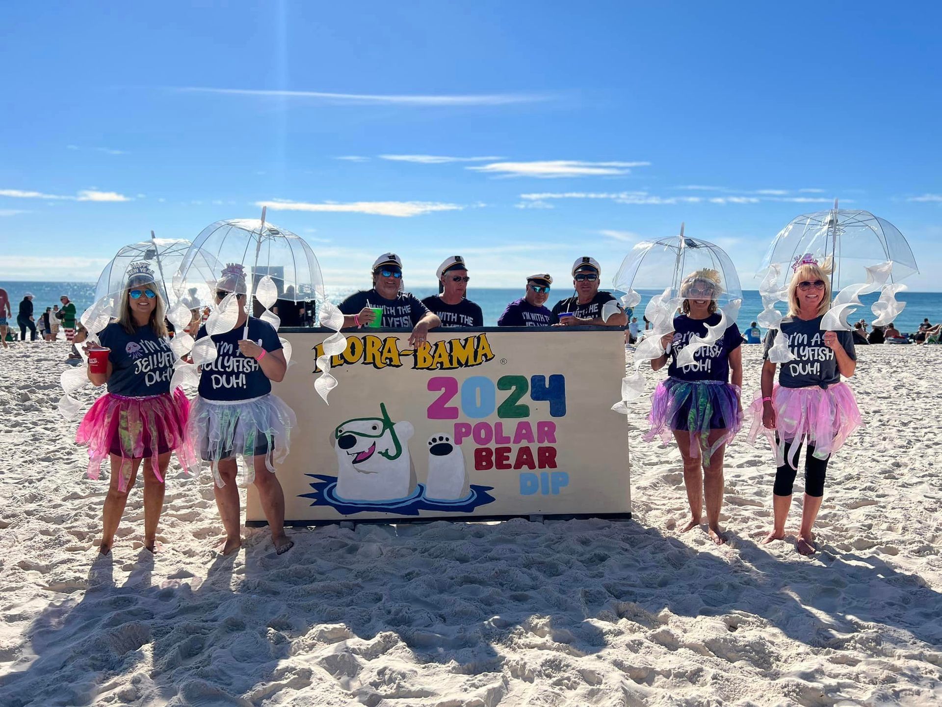 Eight people stand on a sunny beach behind a sign reading