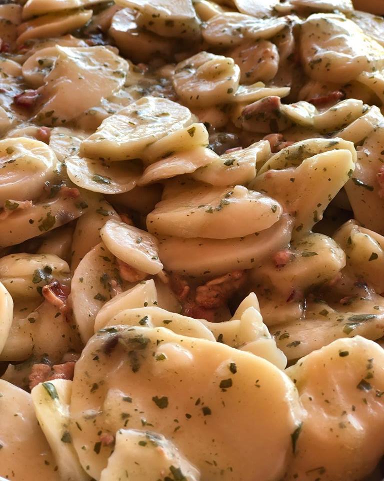 Close-up of sliced potatoes cooked in a creamy sauce with herbs and small pieces of bacon.