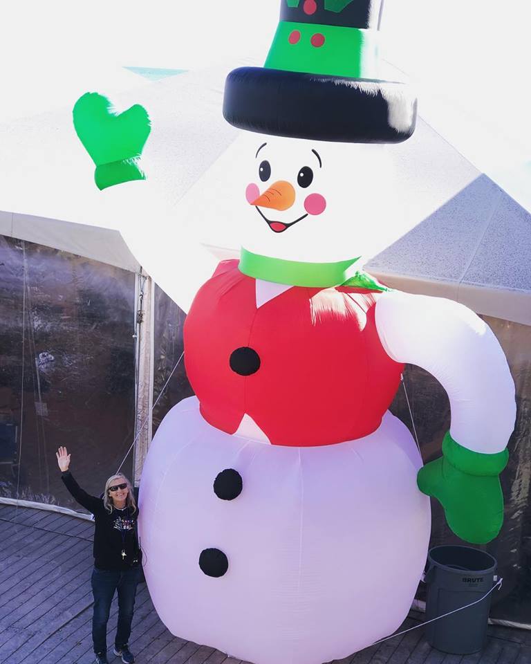 A person standing next to a large, inflatable snowman decoration on an outdoor deck.