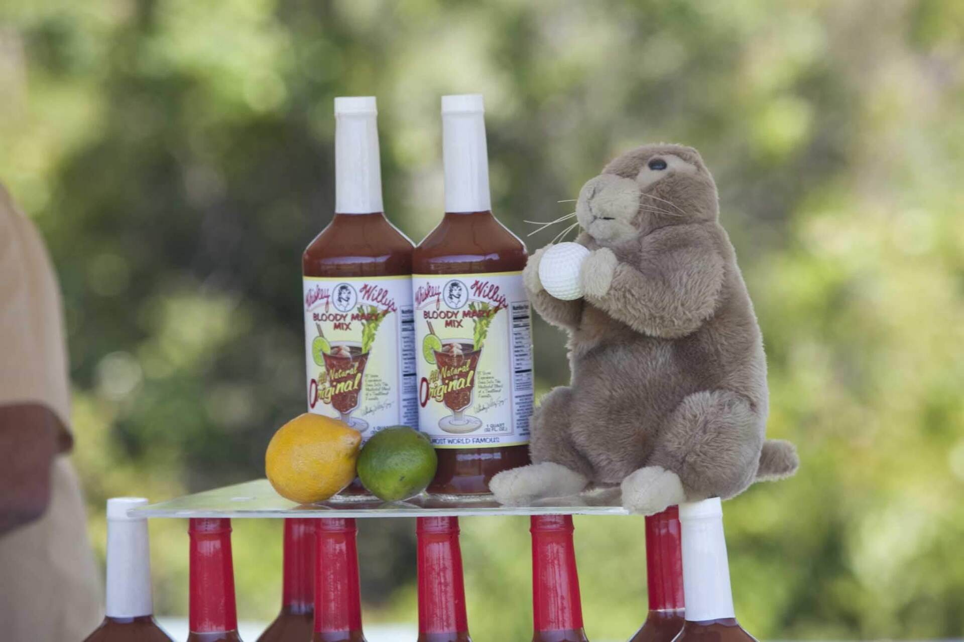 A stuffed groundhog sits next to two bottles of Bloody Mary mix and a lemon and lime on a display of bottle tops.
