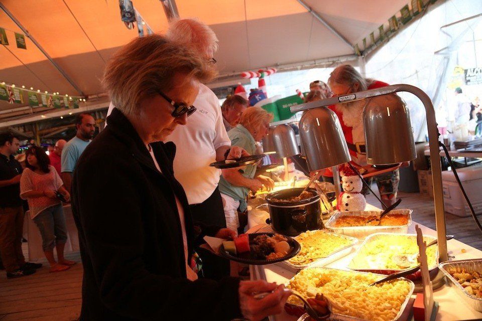People serve themselves food from a buffet line under a tented area.