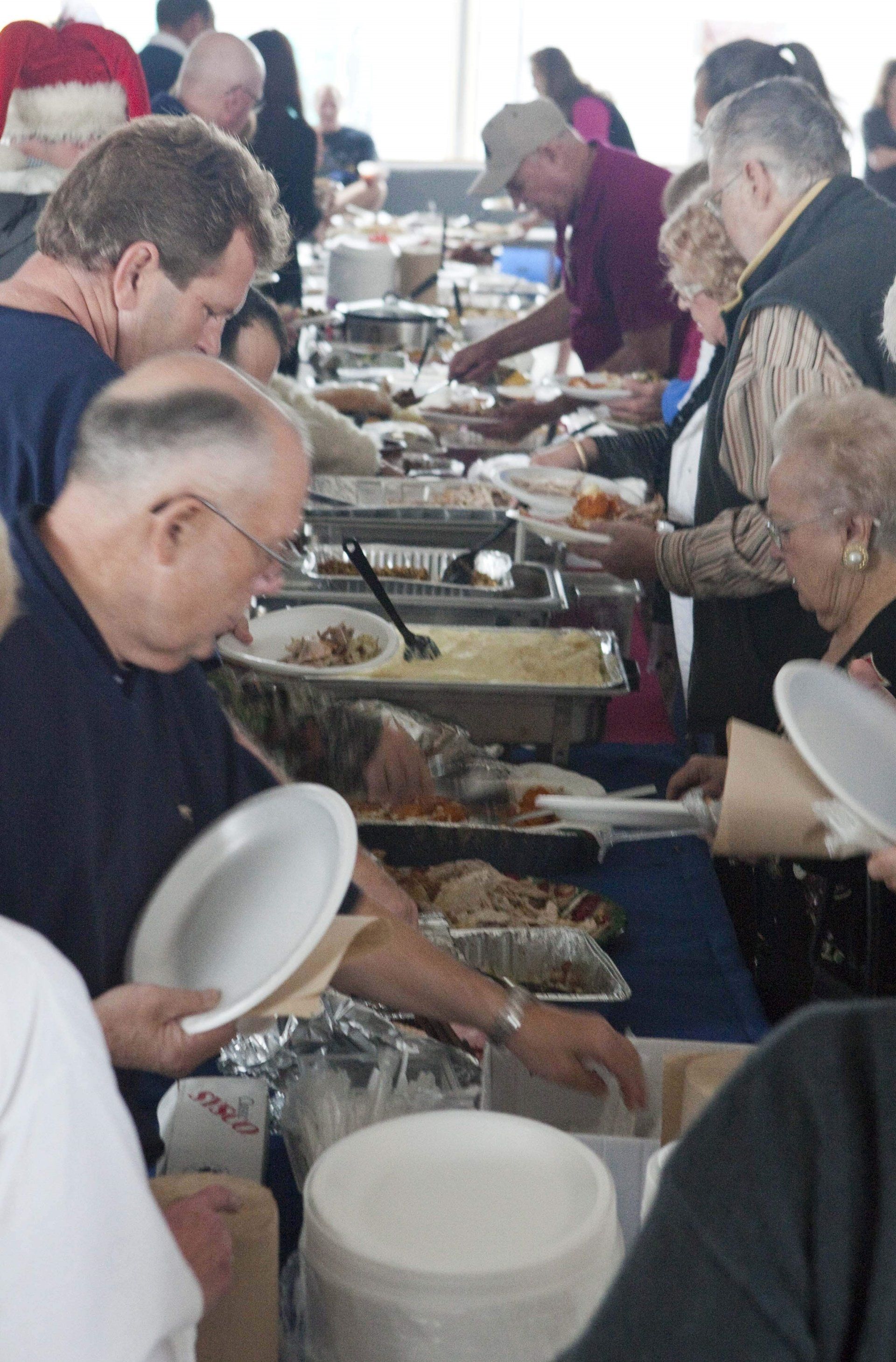 People in a buffet line filling their plates with food from metal serving pans at an indoor event.