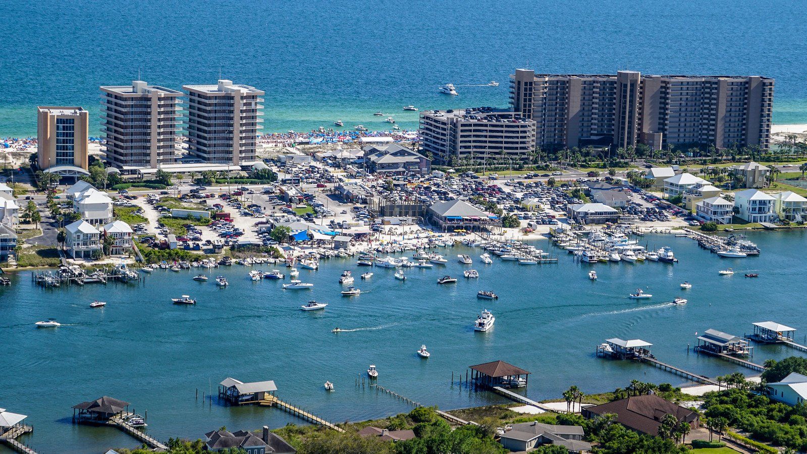An aerial view of a harbor with boats moored at docks, sandy beaches, and large apartment buildings near the ocean.