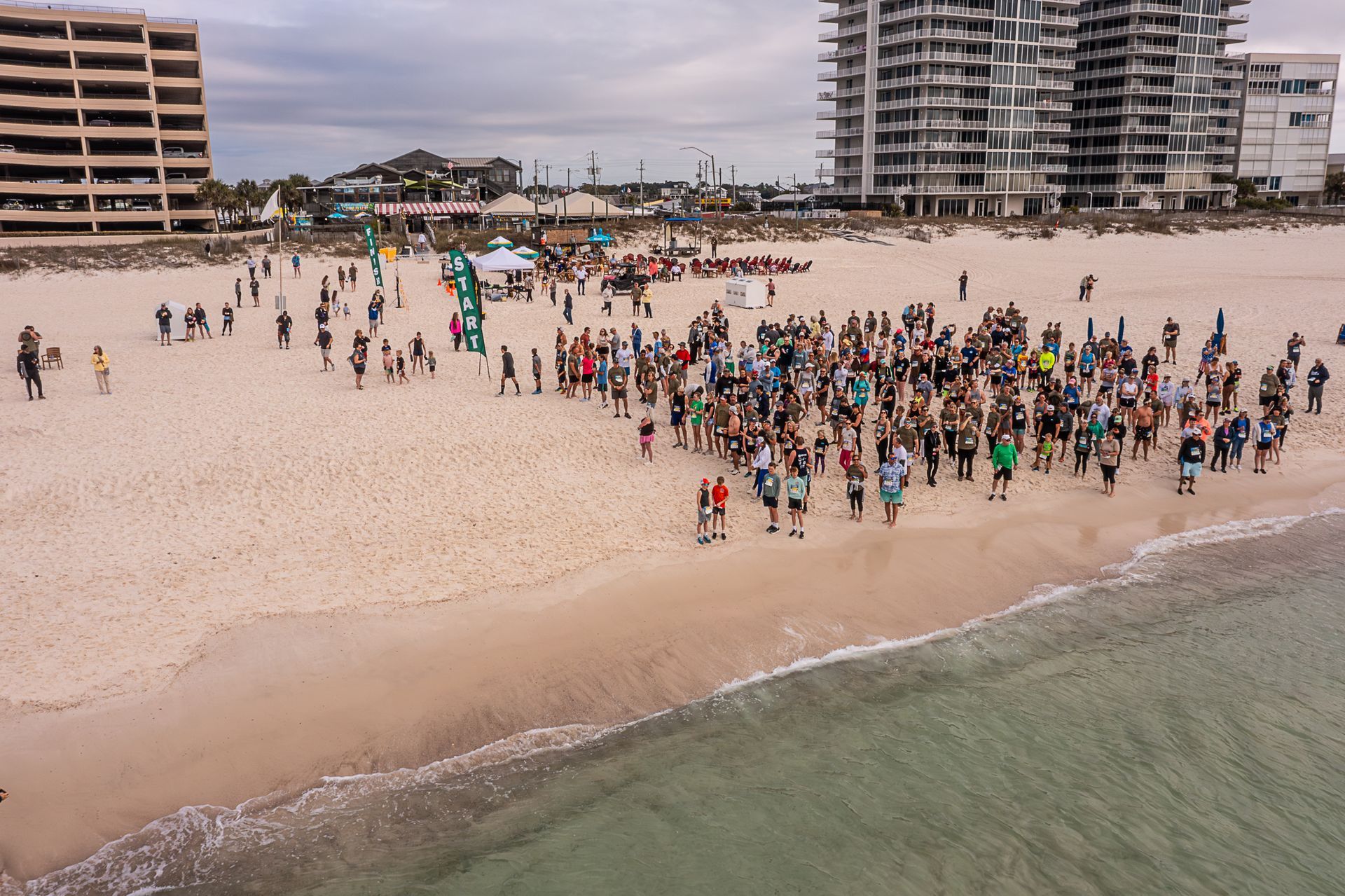 A large group of people gathers on a sandy beach near high-rise buildings during an outdoor event.