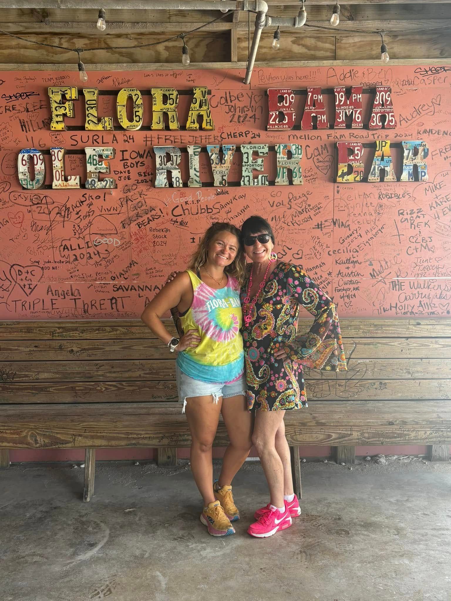 Two smiling people stand in front of a rustic orange wall labeled 