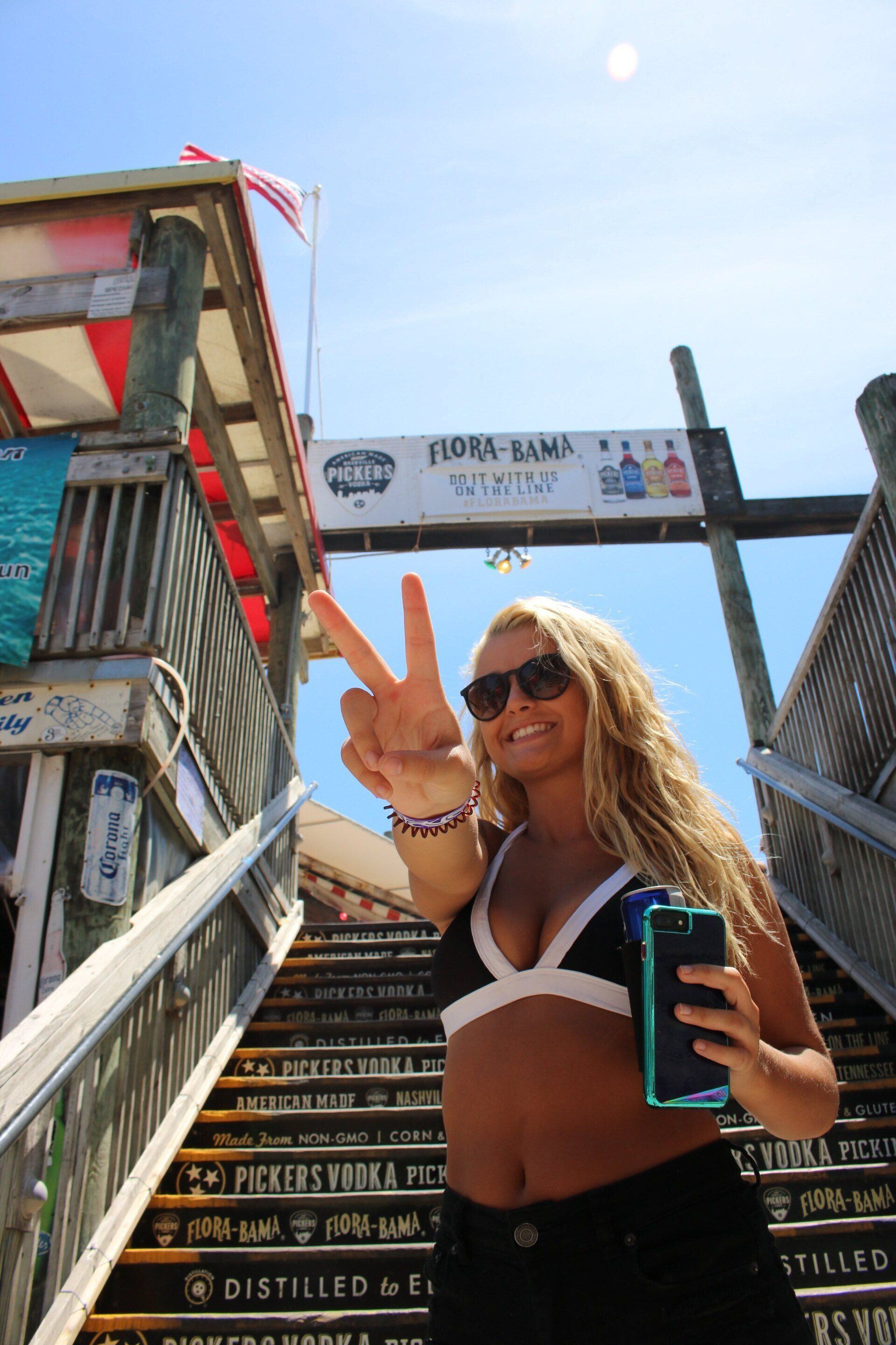 A person smiling and making a peace sign while holding a phone, standing on stairs labeled 